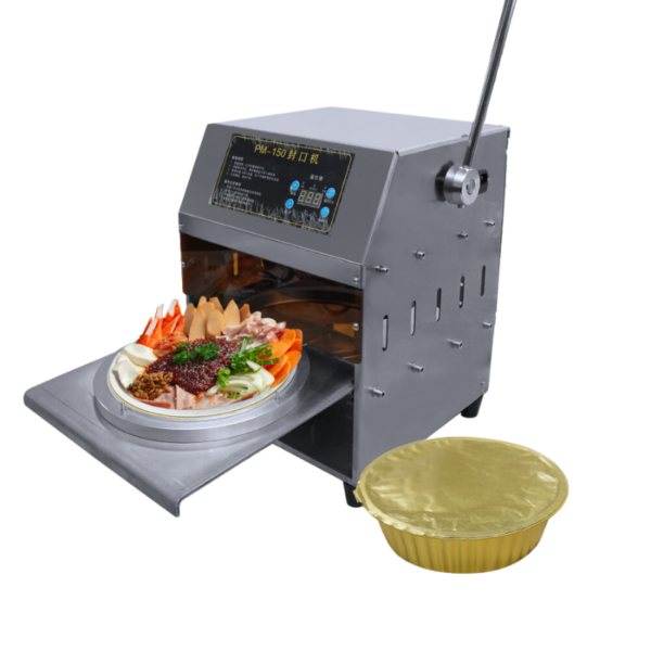 The Round Shape Lunch Box Semi-Auto Sealing Electric Machine Big FLB171 is displayed with an open section containing assorted foods, resembling a high-tech lunch box. Nearby is a separate round golden foil lid ideal for this sealing machine.