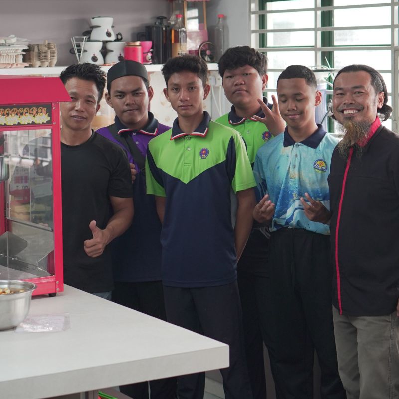 A group of six people standing in a kitchen, with a popcorn machine on the counter. They are smiling and posing for the photo.
