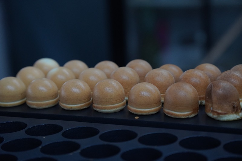 Rows of small, round, golden brown baked pastries are lined up on a black tray, each fitting neatly into separate circular molds of a kayaball machine.