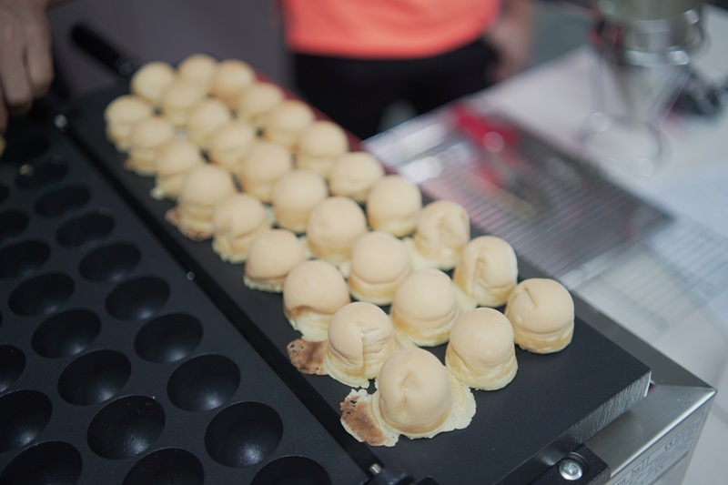 A row of round, golden baked pastries sits on a black Kayaball machine baking mold, with empty circular compartments beside them.