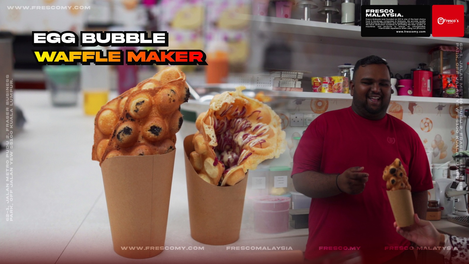 A man in a red shirt holds an egg bubble waffle in a paper cup, with two similar waffles beside him and a Waffle Cone machine visible among the kitchen equipment in the background.