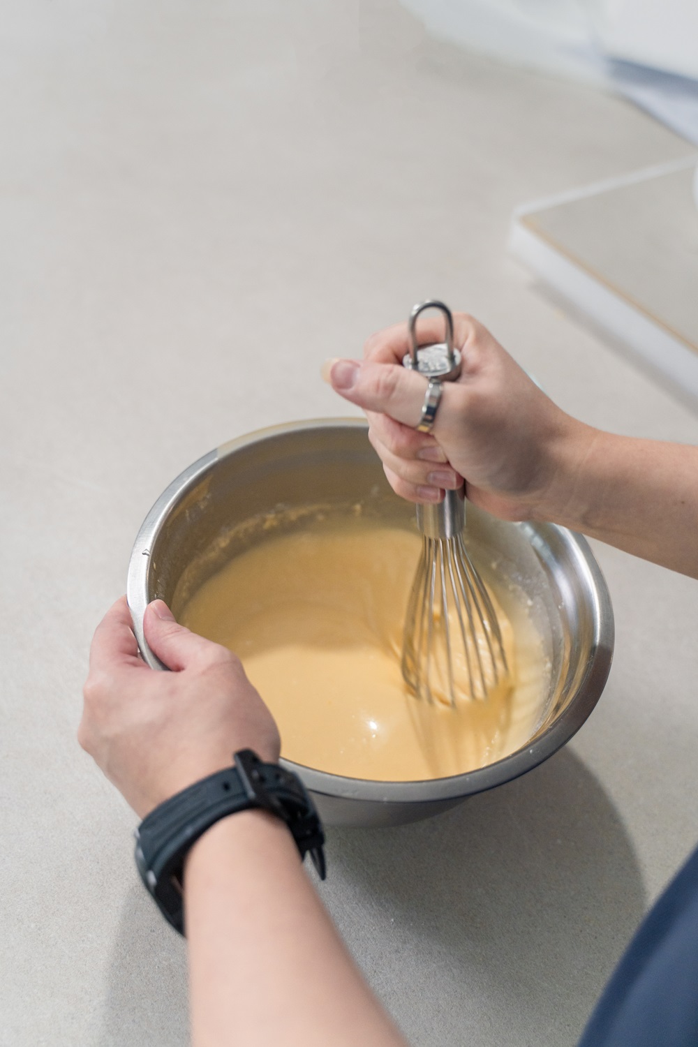 A person whisking a yellow batter in a stainless steel bowl on a light-colored countertop—preparing to use an Egg Waffle Machine, perfect for those looking to Start Small Food Business ventures.