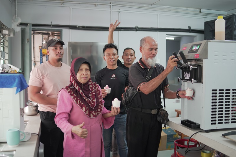 Five people stand together in a kitchen, with one man operating an ice cream maker while the others hold cups and pose for the camera, showing off their pick for the best ice cream machine.