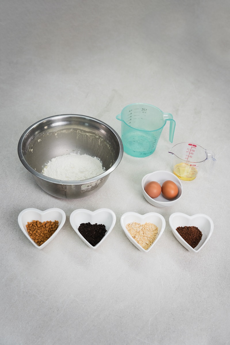 Baking ingredients arranged on a countertop, ready for a crispy waffle balls recipe—flour in a bowl, measuring cup with liquid, two eggs, melted butter, and four heart-shaped bowls filled with different powders.