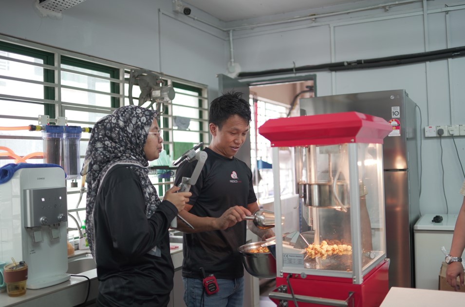 Two people are making popcorn with a Fresco popcorn maker in a kitchen, surrounded by various kitchen equipment and appliances, demonstrating how to make cinema popcorn at home.
