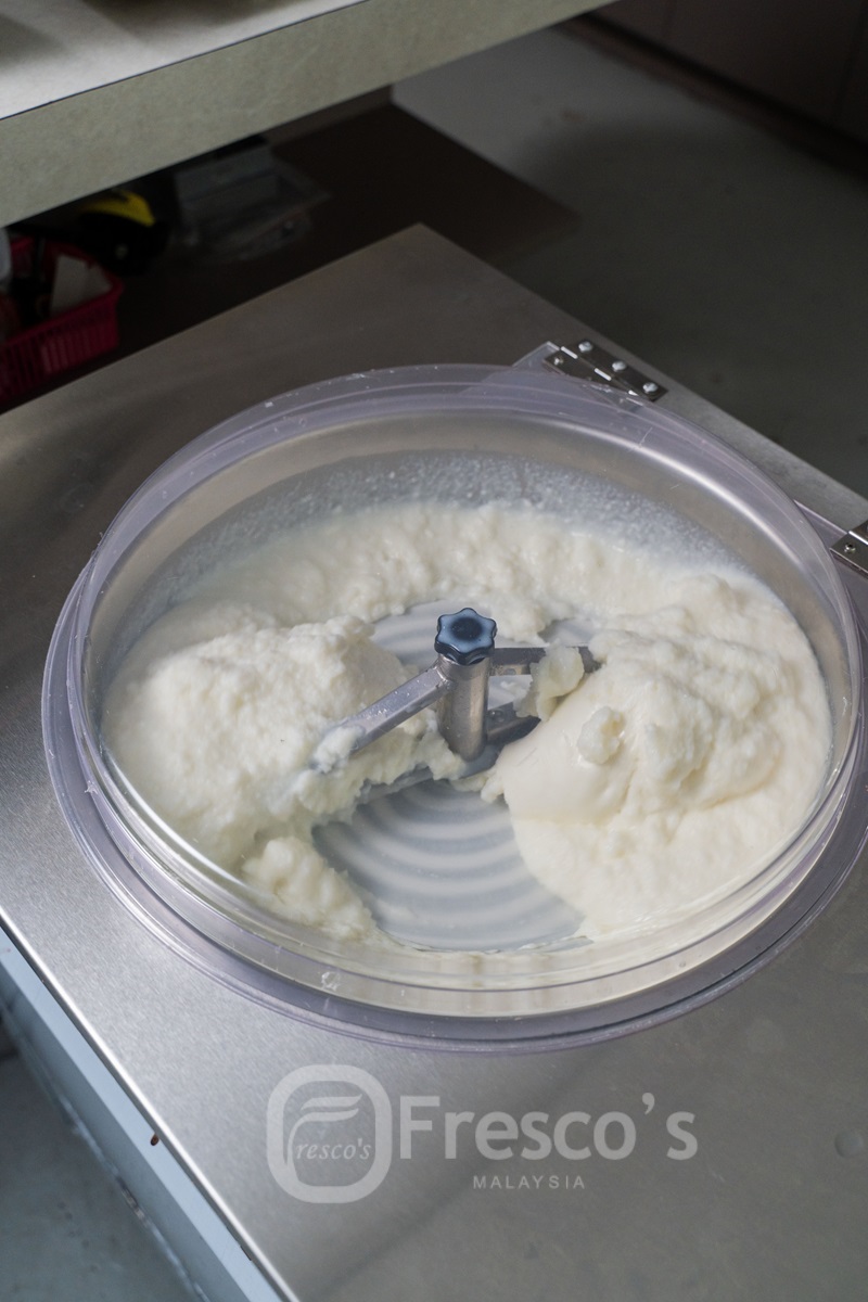 A commercial ice cream and sorbet maker mixing a batch of white frozen dessert, viewed from above, with the Fresco’s Malaysia logo visible on the machine lid.