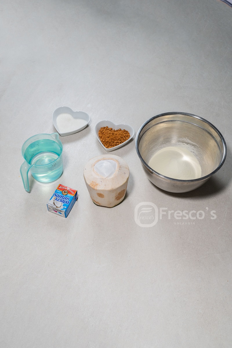 Various ingredients for a frozen dessert are arranged on a light surface, including a metal bowl with liquid, a carton of milk, whole coconut, sugar, coffee granules, and a cup of water—perfect for learning how to make sorbet at home.