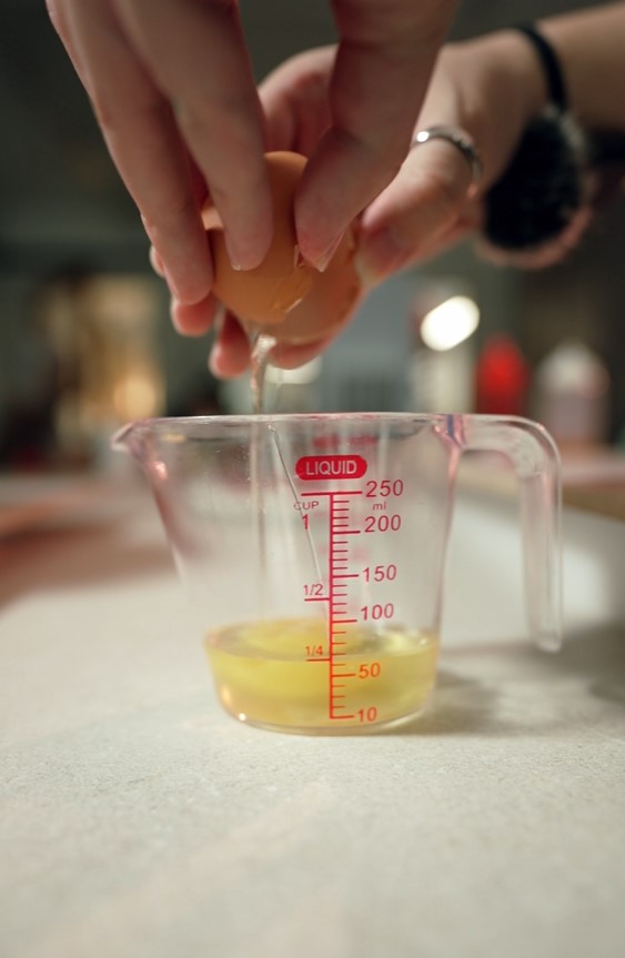 Cracking an egg into a clear measuring cup filled with liquid, this step is perfect for your waffle balls recipe—showing precise measurements up to 250 milliliters.