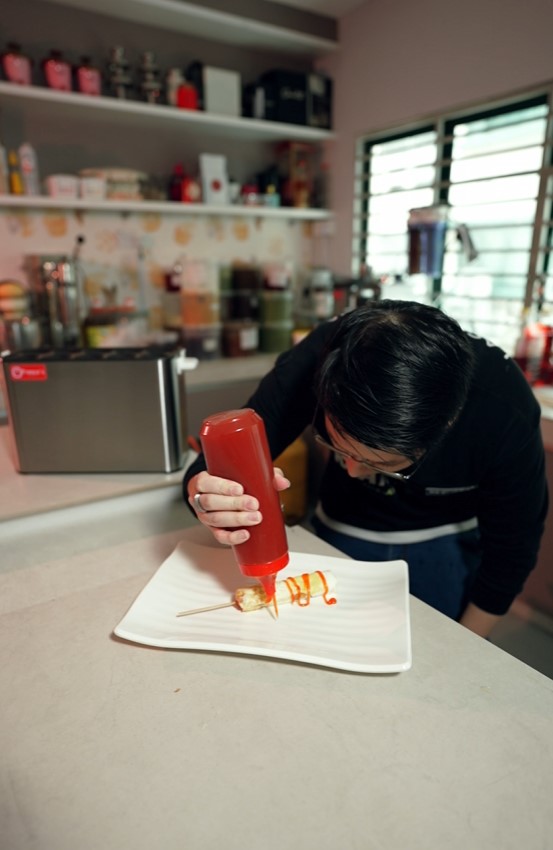 A person decorates food on a white plate with sauce from a squeeze bottle in a kitchen, preparing to serve a delicious waffle ball made fresh from a waffle ball machine.