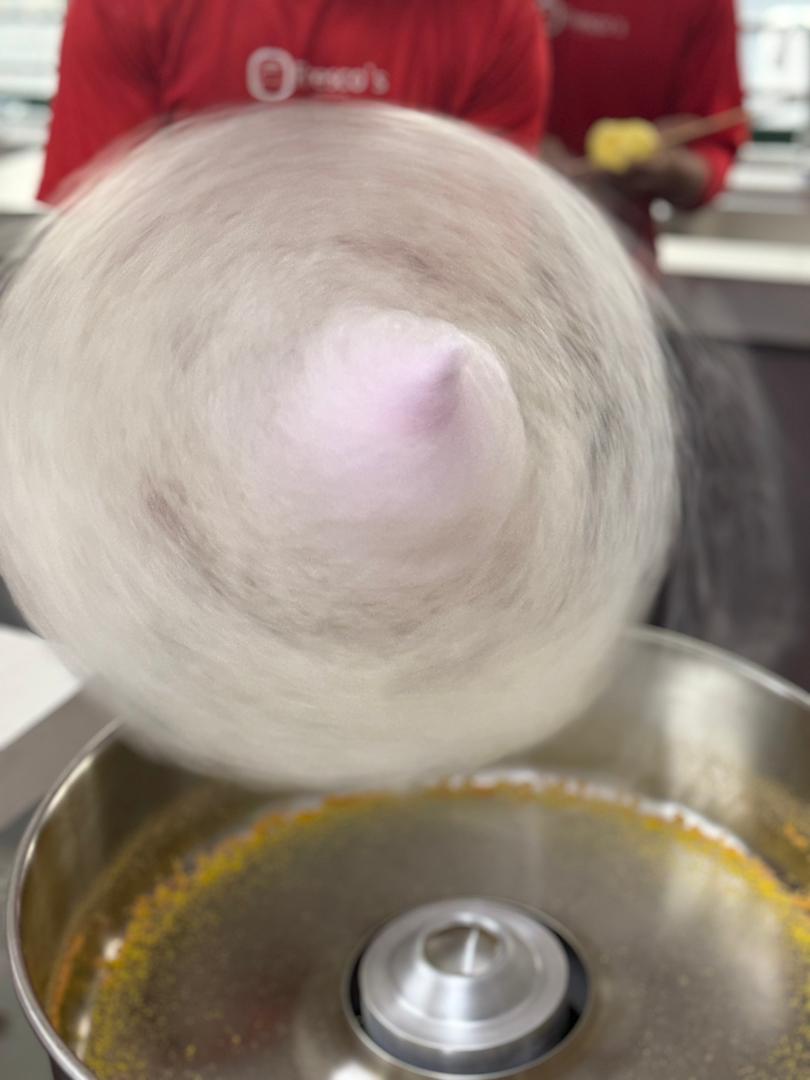 A person in a red shirt spins cotton candy around a stick over a cotton candy machine, with sugar strands swirling in motion during a popcorn machine training session.