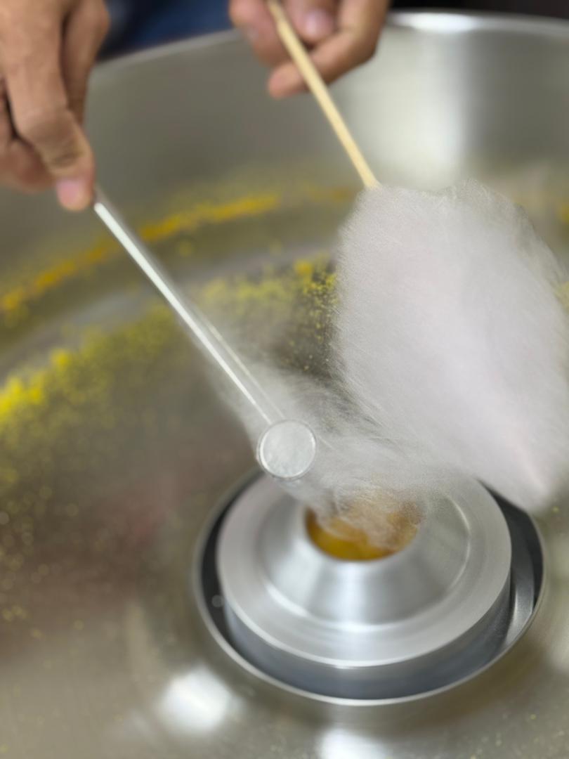A person spins a stick in a cotton candy machine, collecting strands of pink cotton candy around the stick, just like learning in a fun machine tutorial.