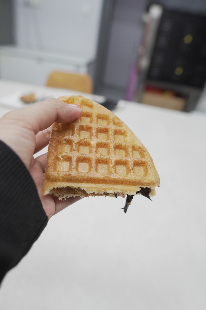 A hand holding a partially eaten waffle with a chocolate filling, made using the best waffle machine, indoors with a blurred background.