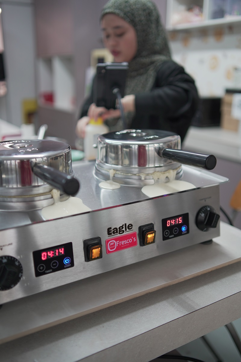 A woman prepares food behind a double-burner Eagle Waffle Machine, with batter spilling from the edges of both burners.