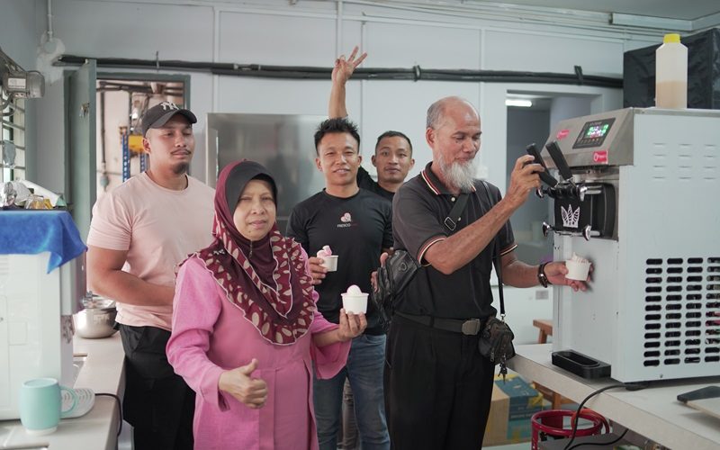 Five people stand together in a kitchen, with one man operating an ice cream maker while the others hold cups and pose for the camera, showing off their pick for the best ice cream machine.